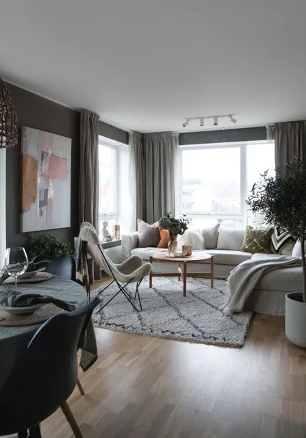 Privatbolig: stue med hjørnesofa, trebord, plante og store vinduer med grå gardiner