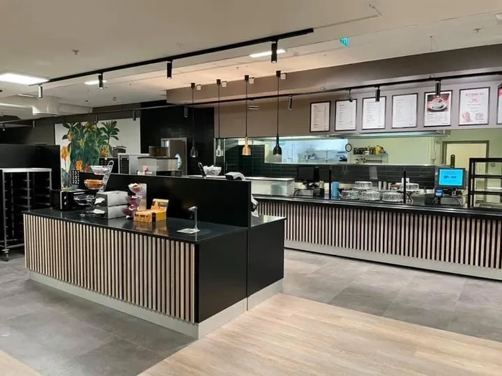 Coop Cafe Steinkjer: serveringsdisk med sort benkeplate og lamellpanel, og innrammede bilder på veggen bak