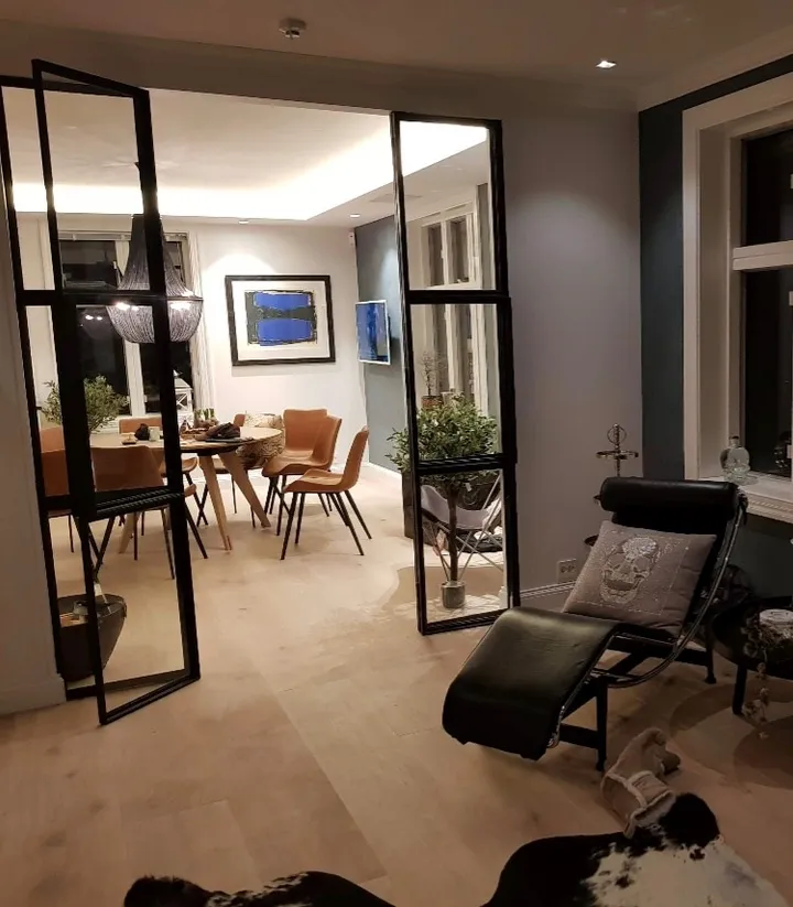 Stue: spiseplass med trestoler bak glassdører og en svart hvilestol i forgrunnen