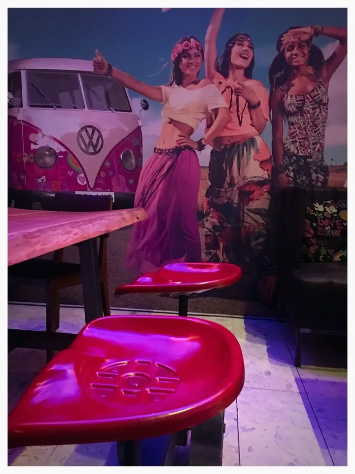 Opland Burger & Steak: rosa barkrakk og treplatebord foran et veggmotiv av dansende mennesker og en Volkswagen-buss