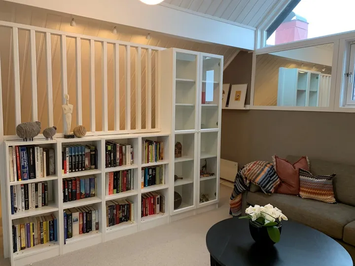 Loftstue: loftsstue med hvit bokhylle, sofa med puter og et rundt svart bord