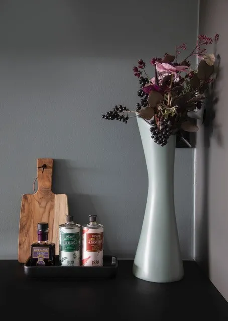 Bonytthjelpen: lysegrønn vase med tørkede blomster og et skjærebrett mot en grå vegg