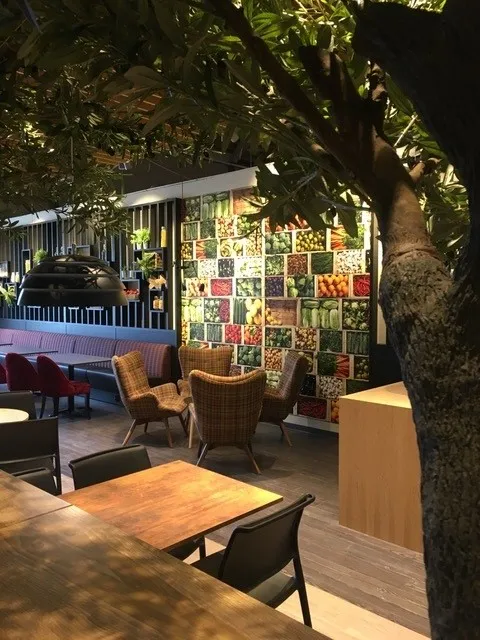 Coop Cafe Rudshøgda: spisesal med røde sofaer, rutete lenestoler og et veggmotiv av frukt og grønnsaker bak et stort tre
