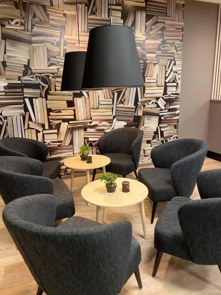 Coop Cafe Steinkjer: grå lenestoler og små runde bord foran en vegg med bokhyllemotiv