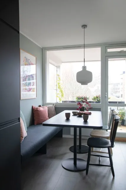 Bonytthjelpen: spiseplass med sort bord, benk med rosa puter og store vinduer med pendellampe
