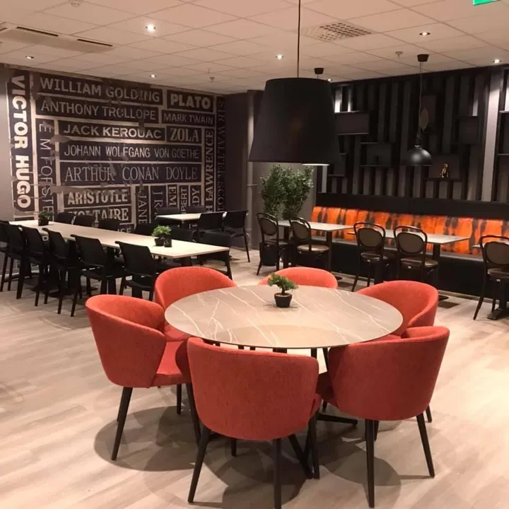 Coop Cafe Steinkjer: runde bord med røde stoler og en vegg dekket av forfatternavn i stor skrift