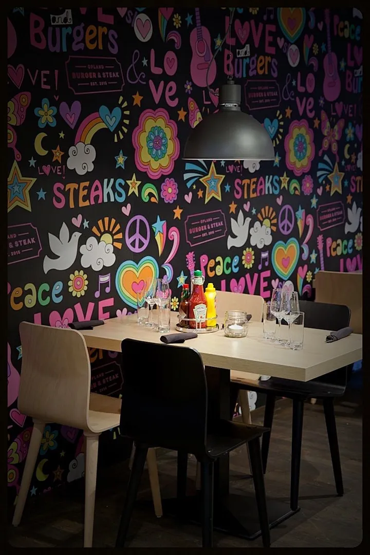Opland Burger & Steak: svart vegg med fargerike fredsmotiver og teksten «Steaks», med et dekket bord foran