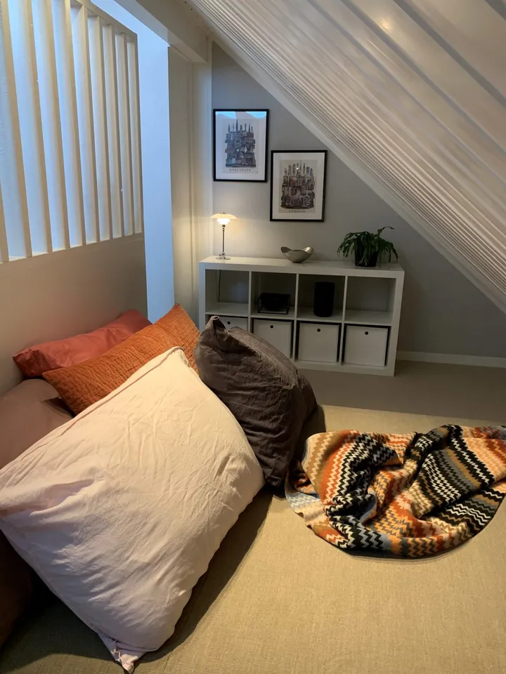 Loftstue: sovekrok under skråtak med puter, pledd og en hvit hylle