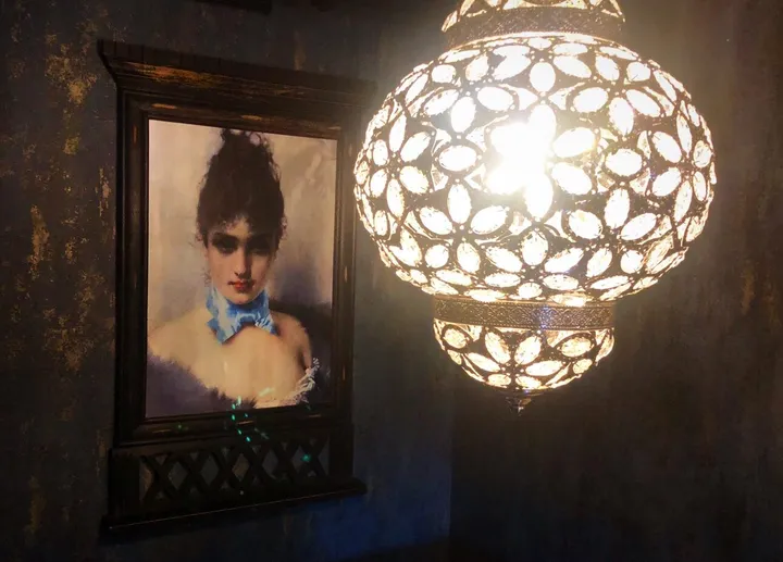 Restaurant Alma – Tønsberg: innrammet portrett av en kvinne ved siden av en ornamentert lampe
