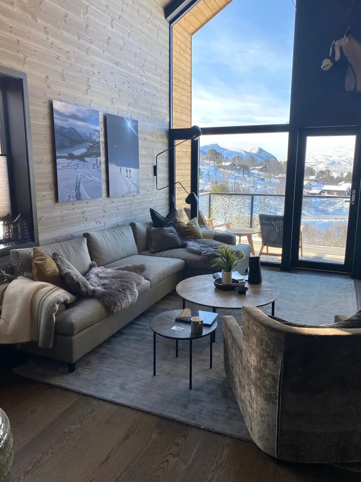 Fritidsleilighet Hovden: stue med sofa, runde bord og fjellmotiv på veggen, med utsikt mot snødekte fjell