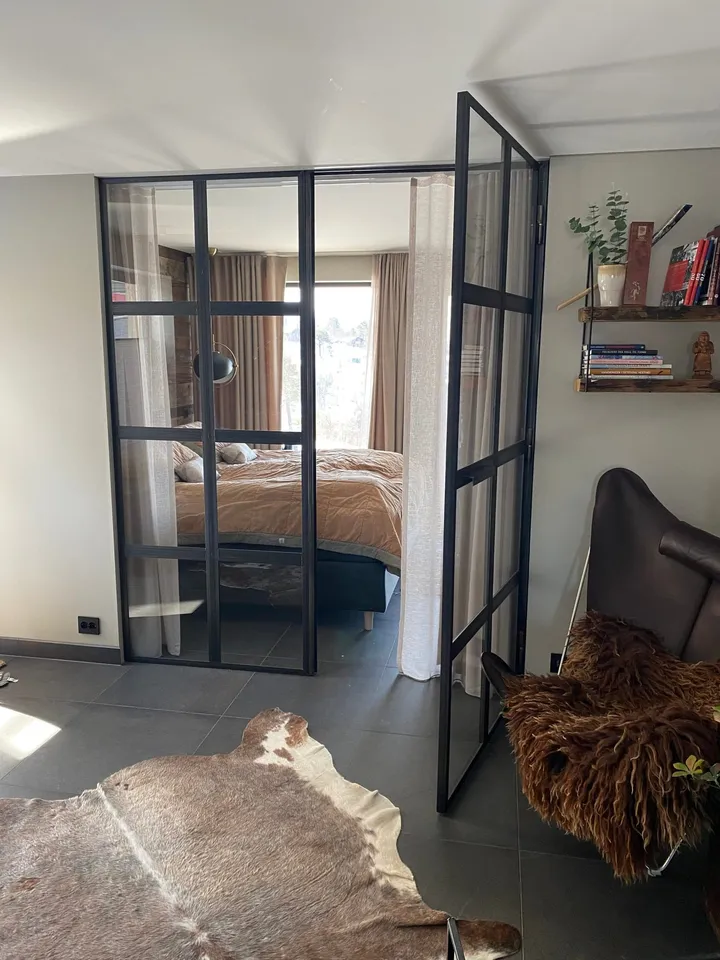 Fritidsleilighet Hovden: soverom bak glassvegg med svart ramme og en lenestol med skinn i forgrunnen
