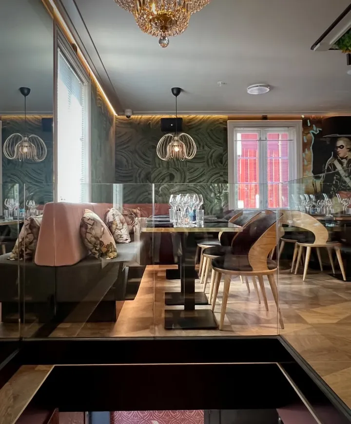 Alma restaurant: lyst lokale med rosa sofa, puter, trebord og stoler foran en mønstret grønn vegg