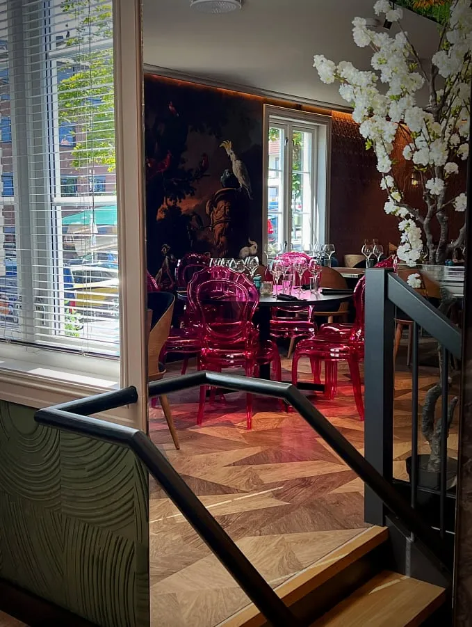 Alma restaurant: spisesal med rosa gjennomsiktige stoler, fiskebensparkett og blomstrende grener ved vinduet