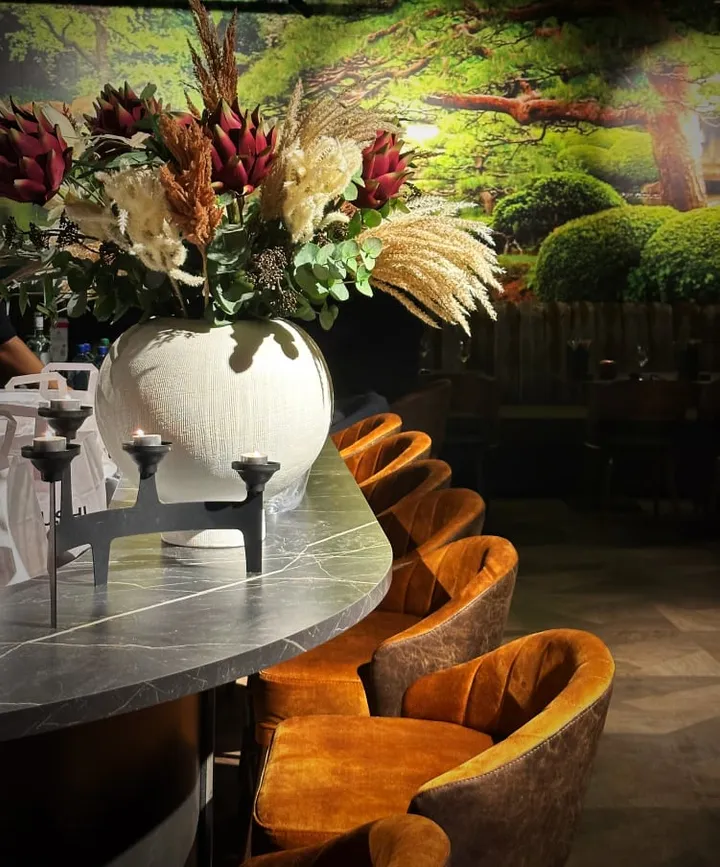 Japo Sushi: hvit vase med tørkede blomster og lysestake på et marmorbord med oransje fløyelsstoler