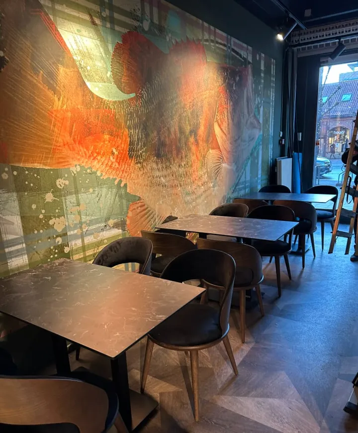 Japo Sushi: spisesal med sorte bord og stoler foran en vegg med oransje og rødt motiv