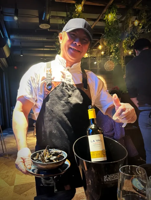 Japo Sushi: person i hvit skjorte og svart forkle som holder en vinflaske