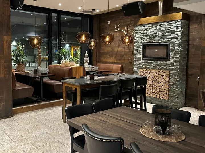 Crosta Restaurant Alta: spisesal med mørke trebord, skinnstoler, kobberpendler og en peisvegg av skifer med vedkubber