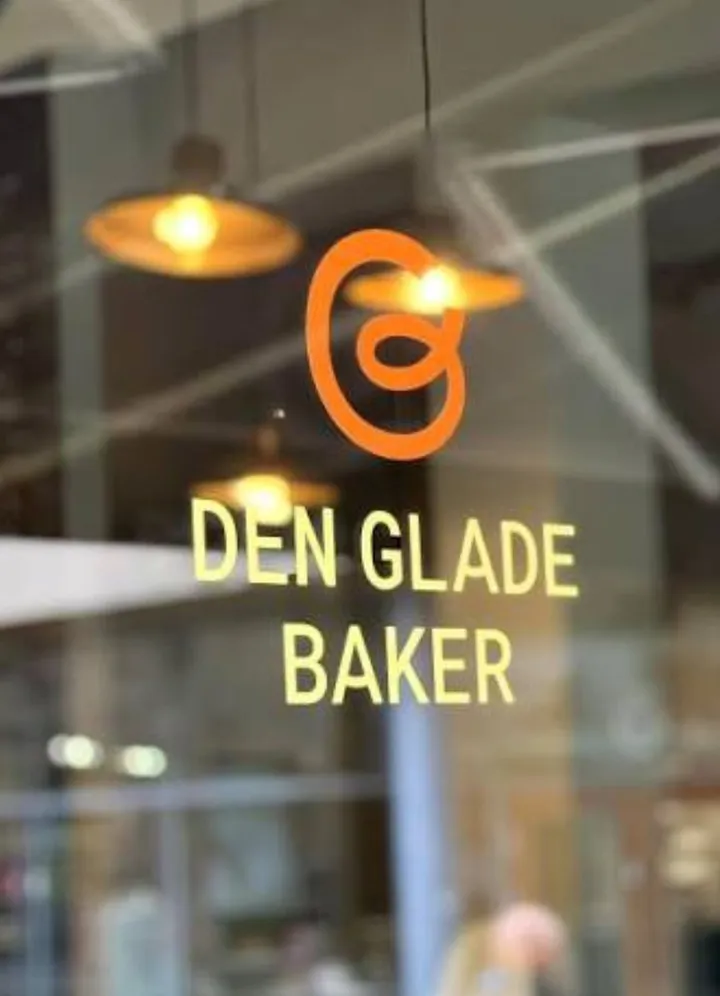Den glade baker – Asker: logoen og navnet «Den glade baker» på en glassvegg, med pendellamper som speiles i glasset