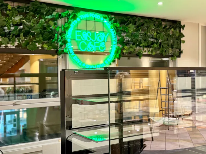 Enjoy Cafe – Hammerfest: grønt neonskilt med teksten «Enjoy Cafe» i en vegg av grønne planter over en glassmonter